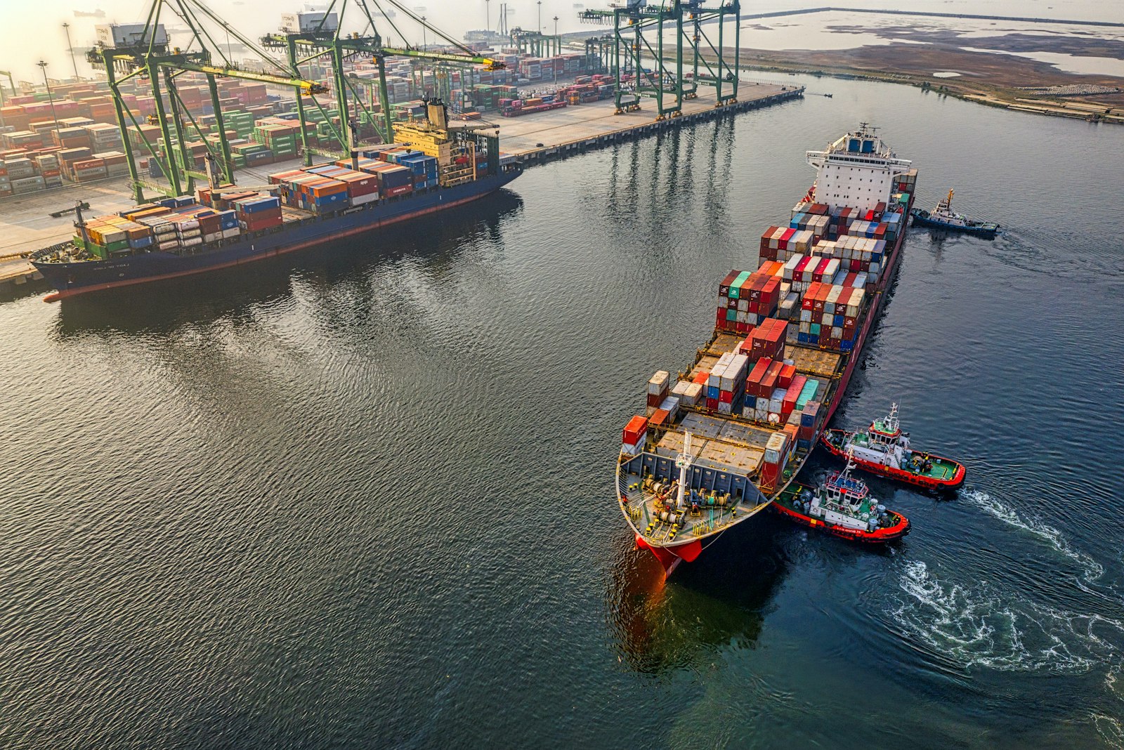 Aerial view of a container vessel guided by tugs into a terminal